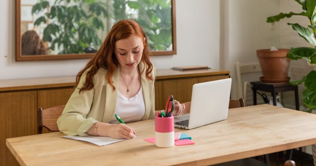 Woman drafting blog post notes at a wooden desk with laptop, planning ecommerce content that links to products