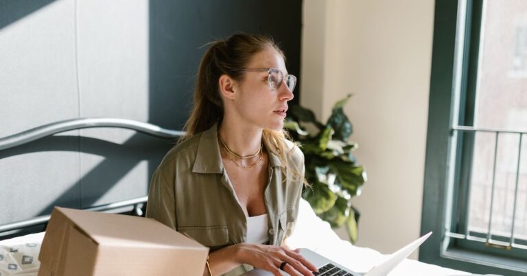 Online store owner working on a laptop beside a shipping box, managing her Shopify store from home